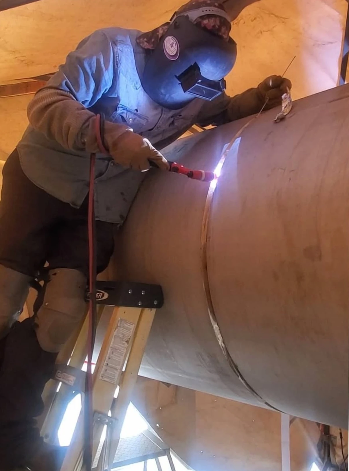 Travis Field welding a large-diameter pipe joint from a ladder