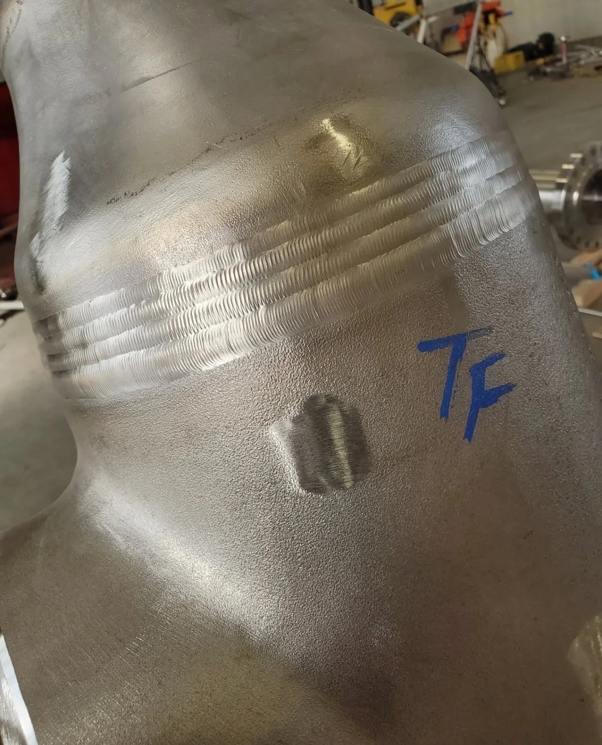 Wide multi-pass weld on a pipe fitting with a blue TF marking